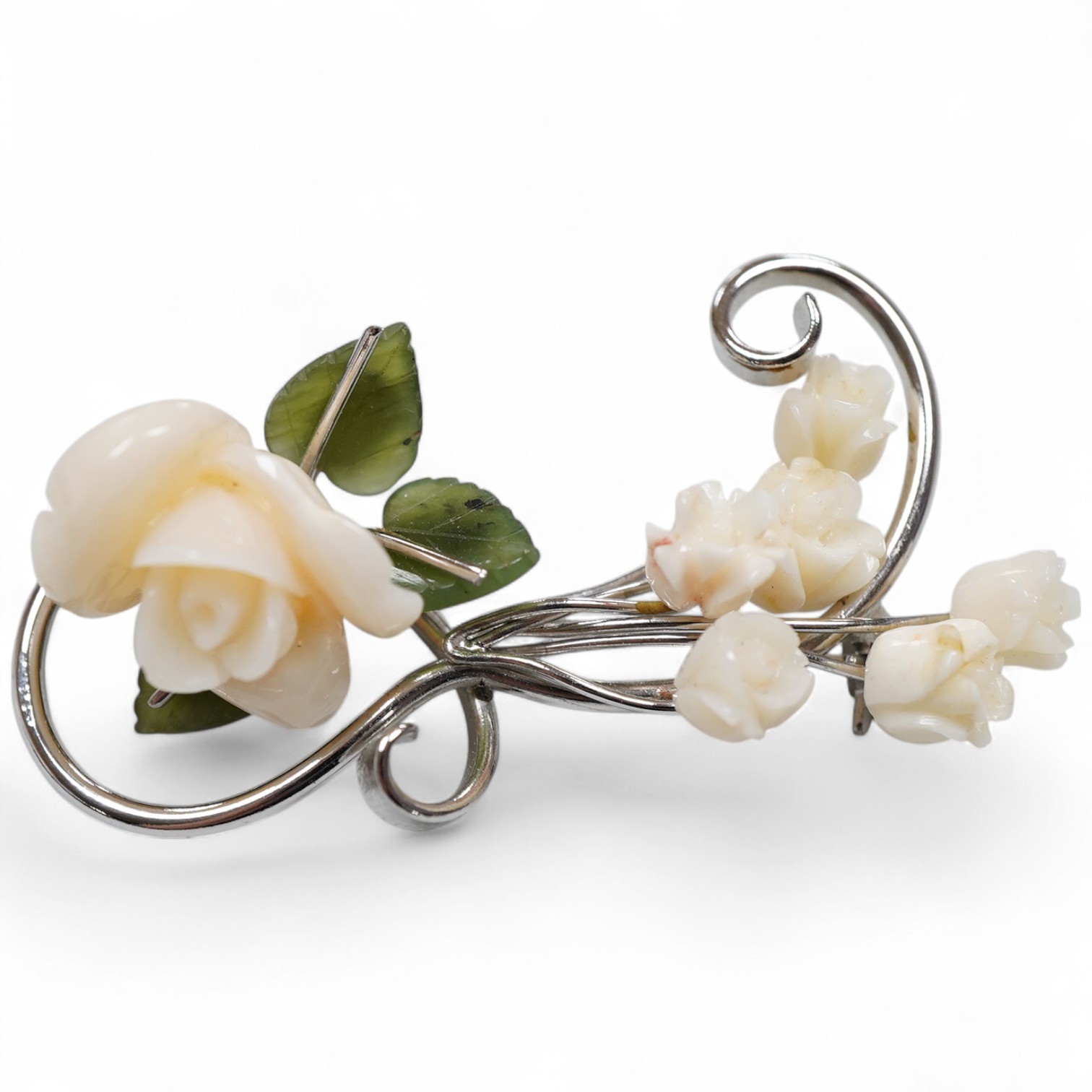 A white coral and nephrite brooch, designed as a spray of roses in carved white coral with nephrite leaves, on a scrolled white gold mount, length 5.5cm, stamped 14K, gross weight 11 grams